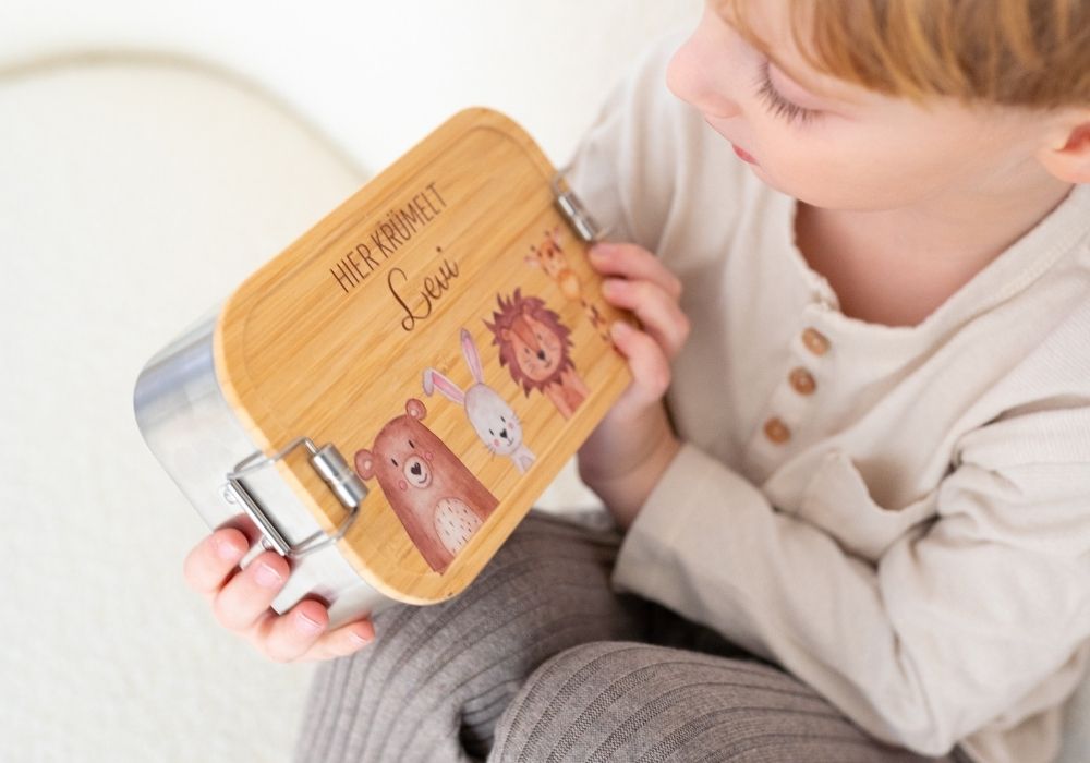 Kind hält personalisierte Brotdose mit Bambusdeckel, Tiermotiven und Namen Levi